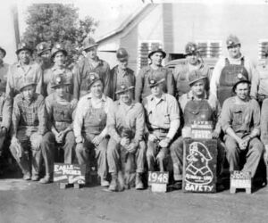 Mining crews posed for annual photo in front of the "dog house" where they changed their clothes. Mutt Mantle is seen in the light colored baseball cap on both ends of the photo. The exposure was so slow he had time to run from one end of the lineup to the other.